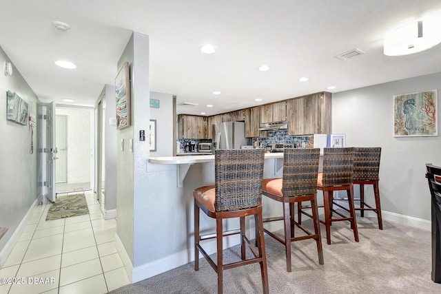 kitchen with tasteful backsplash, stainless steel fridge with ice dispenser, a kitchen breakfast bar, and kitchen peninsula