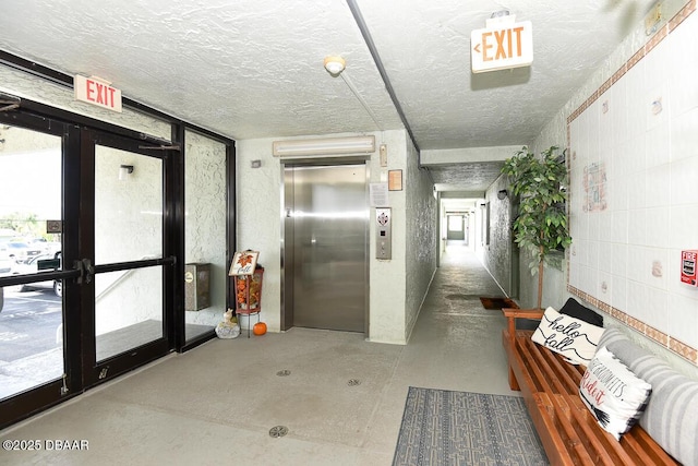 corridor with elevator, a textured ceiling, and french doors