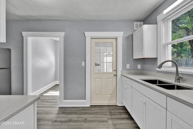 kitchen with sink, light stone countertops, white cabinetry, light hardwood / wood-style flooring, and stainless steel fridge