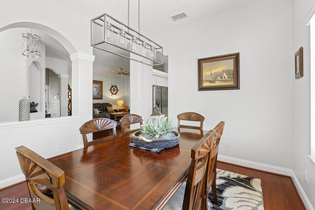 dining room with wood-type flooring, ceiling fan with notable chandelier, and decorative columns