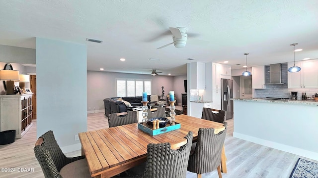 dining space with a textured ceiling, light wood-style flooring, visible vents, and baseboards