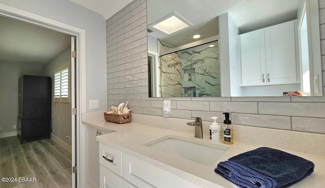 full bath featuring a marble finish shower, tasteful backsplash, vanity, wood finished floors, and baseboards