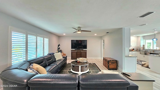 living room with light wood-style floors, baseboards, visible vents, and a ceiling fan