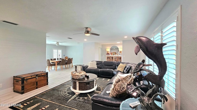 living area with a ceiling fan, wood finished floors, visible vents, and baseboards