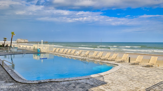 view of pool with a beach view, a water view, and a patio