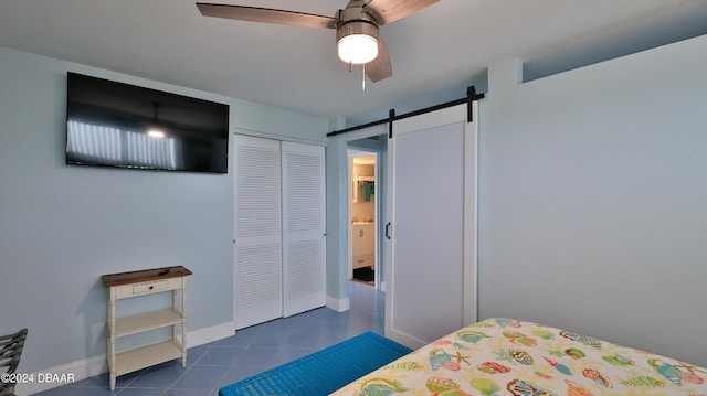 tiled bedroom with a barn door, ceiling fan, and a closet