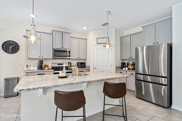 kitchen with an island with sink, gray cabinetry, light stone counters, and appliances with stainless steel finishes