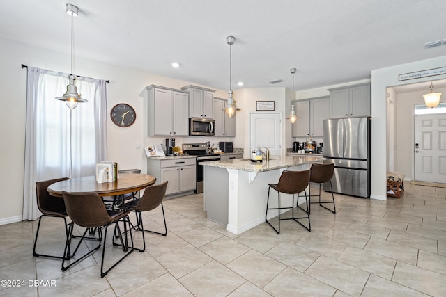 kitchen with appliances with stainless steel finishes, a kitchen breakfast bar, light stone countertops, a kitchen island with sink, and gray cabinetry