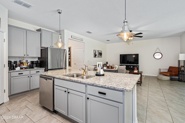 kitchen featuring stainless steel appliances, a center island with sink, sink, gray cabinetry, and pendant lighting