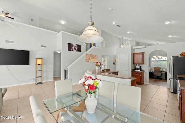 dining room featuring sink, light tile patterned flooring, ceiling fan with notable chandelier, and high vaulted ceiling