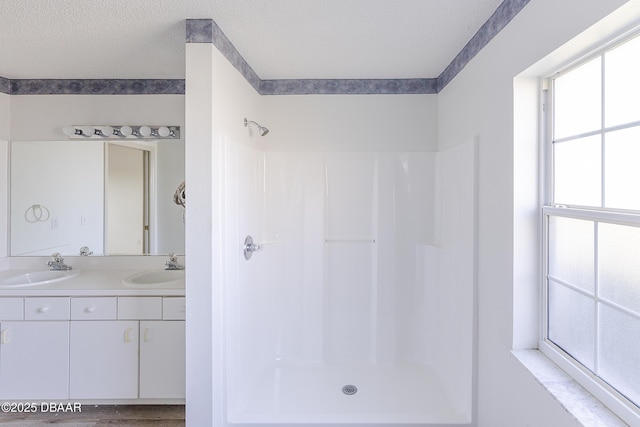 bathroom featuring a textured ceiling, double vanity, walk in shower, and a sink