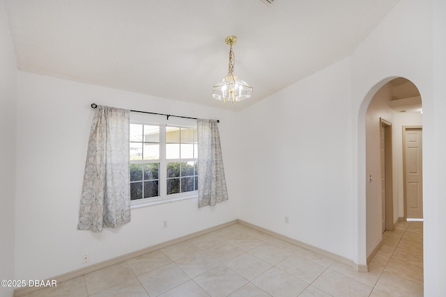 empty room with vaulted ceiling, light tile patterned flooring, baseboards, and arched walkways