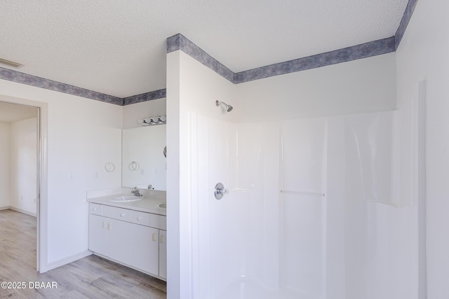 full bathroom with visible vents, a sink, a textured ceiling, wood finished floors, and walk in shower