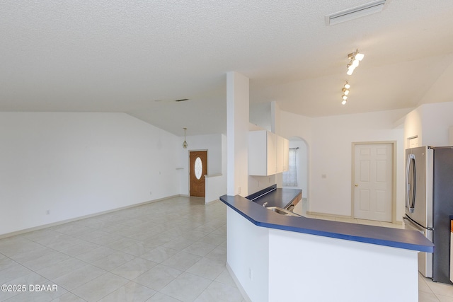 kitchen with lofted ceiling, arched walkways, freestanding refrigerator, dark countertops, and open floor plan