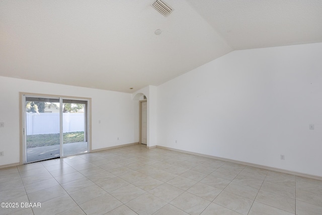 spare room with light tile patterned floors, visible vents, baseboards, arched walkways, and vaulted ceiling