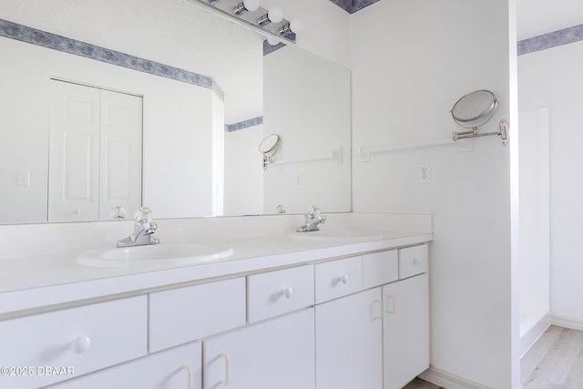 full bath featuring double vanity, wood finished floors, baseboards, and a sink