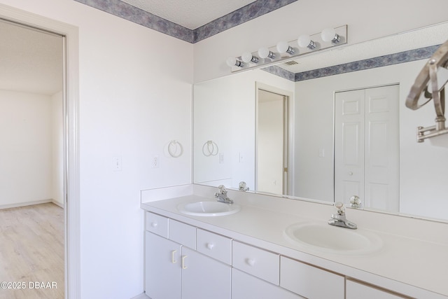 full bath with a sink, a textured ceiling, wood finished floors, and double vanity