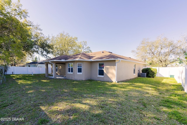 back of house with stucco siding, a yard, central AC unit, and a fenced backyard