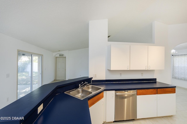 kitchen featuring stainless steel dishwasher, dark countertops, arched walkways, and a sink