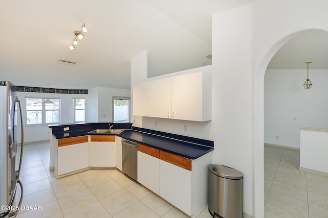 kitchen with a sink, dark countertops, arched walkways, appliances with stainless steel finishes, and light tile patterned floors