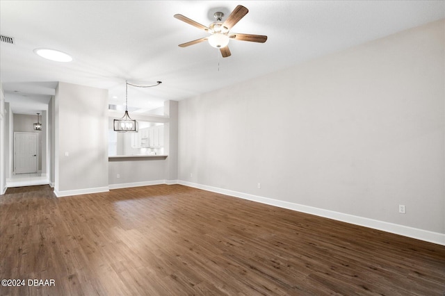 empty room with ceiling fan with notable chandelier and dark hardwood / wood-style flooring