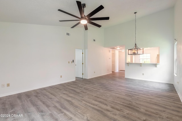 unfurnished living room with high vaulted ceiling, ceiling fan with notable chandelier, and hardwood / wood-style flooring