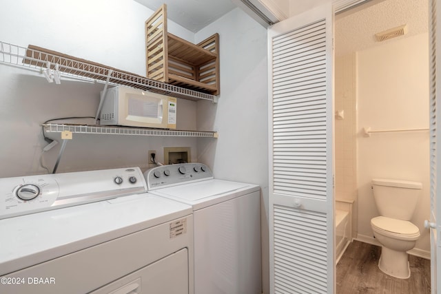 laundry room with washing machine and clothes dryer and hardwood / wood-style flooring