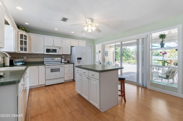 3167 S Peninsula Dr, Daytona Beach, FL 32118 - kitchen featuring visible vents, a sink, dark countertops, white appliances, and a breakfast bar area
