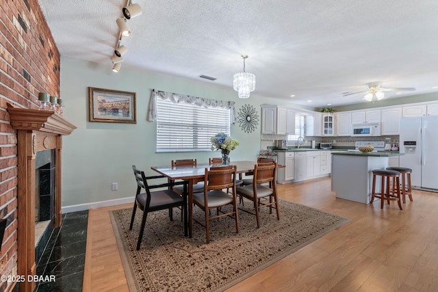 3167 S Peninsula Dr, Daytona Beach, FL 32118 - dining room with ceiling fan with notable chandelier, a textured ceiling, light wood-style floors, a fireplace, and baseboards