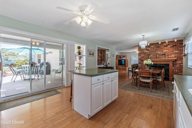 3167 S Peninsula Dr, Daytona Beach, FL 32118 - kitchen with visible vents, dark countertops, white cabinetry, a fireplace, and light wood finished floors