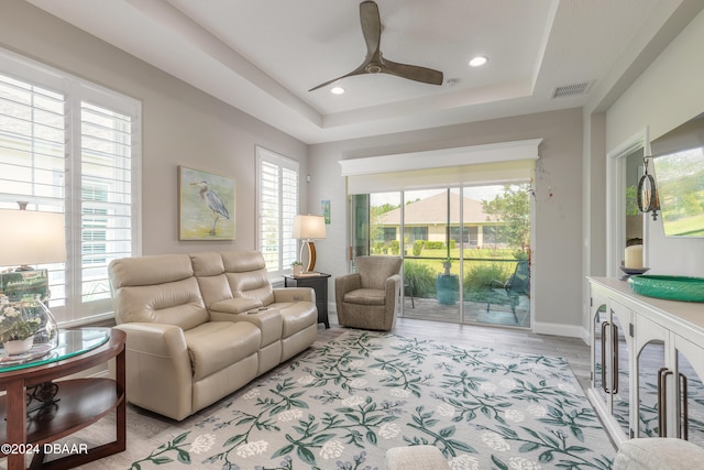 living room featuring ceiling fan, light wood-type flooring, and a tray ceiling