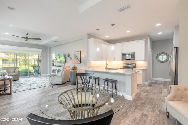 kitchen with light wood-type flooring, white cabinetry, appliances with stainless steel finishes, hanging light fixtures, and kitchen peninsula