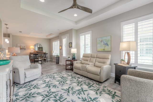 living room with light hardwood / wood-style floors, ceiling fan, and a raised ceiling