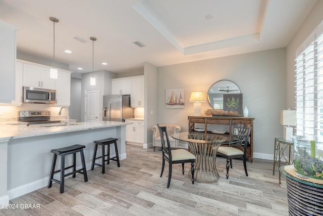 kitchen featuring stainless steel appliances, white cabinetry, sink, light wood-type flooring, and pendant lighting