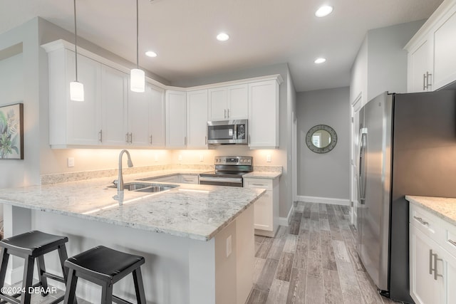 kitchen with appliances with stainless steel finishes, pendant lighting, sink, kitchen peninsula, and light hardwood / wood-style flooring