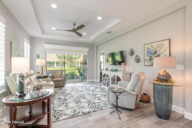 living room with hardwood / wood-style flooring, ceiling fan, and a tray ceiling