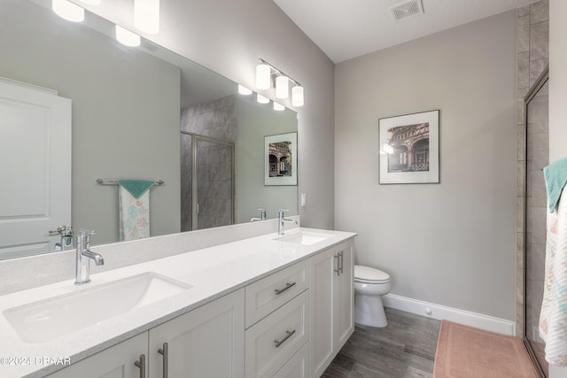 bathroom with a textured ceiling, hardwood / wood-style floors, vanity, a shower with shower door, and toilet