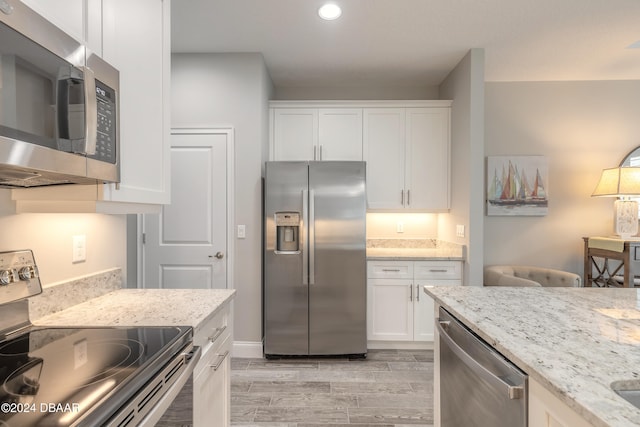 kitchen with white cabinetry, appliances with stainless steel finishes, light stone countertops, and light hardwood / wood-style flooring