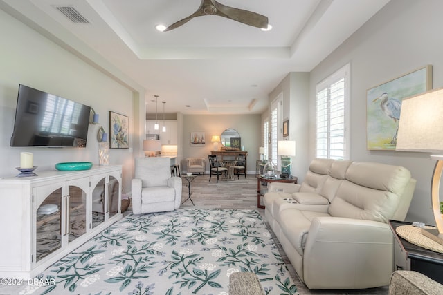 living room featuring light hardwood / wood-style flooring, ceiling fan, and a raised ceiling