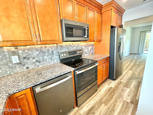 kitchen with decorative backsplash, appliances with stainless steel finishes, light hardwood / wood-style floors, and light stone counters