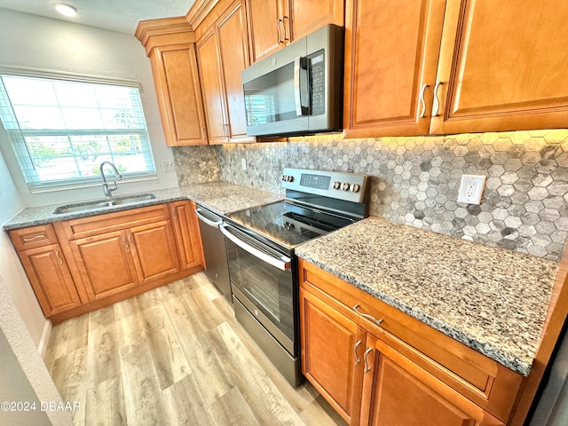 kitchen featuring light hardwood / wood-style floors, light stone counters, sink, tasteful backsplash, and appliances with stainless steel finishes