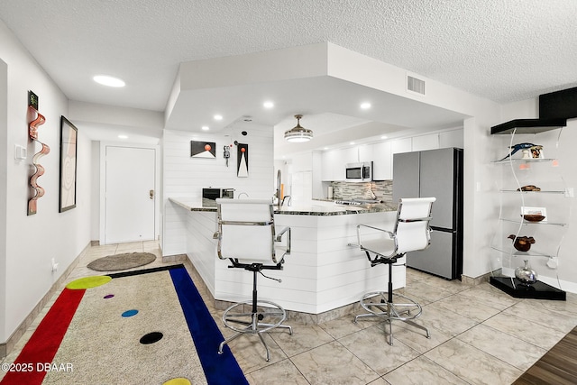 kitchen featuring a breakfast bar, appliances with stainless steel finishes, kitchen peninsula, decorative backsplash, and white cabinets