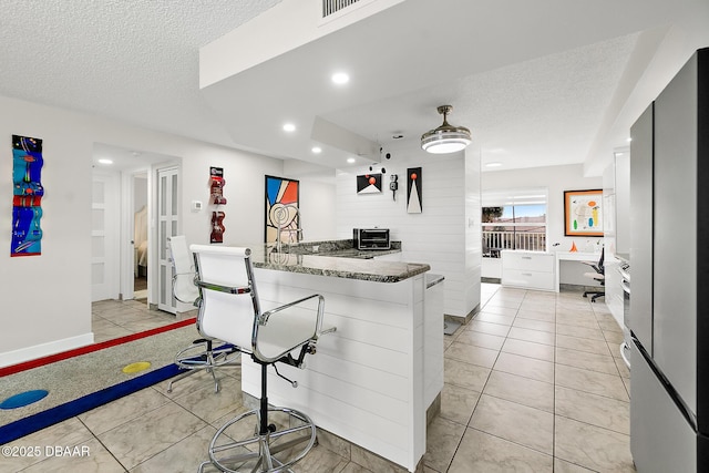 kitchen featuring white cabinetry, dark stone countertops, a kitchen breakfast bar, kitchen peninsula, and a textured ceiling