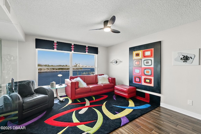 living room featuring a water view, dark wood-type flooring, a textured ceiling, and ceiling fan