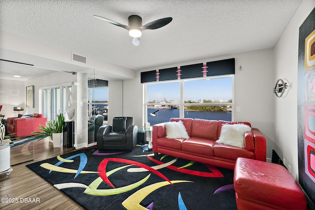 living room with hardwood / wood-style floors, a textured ceiling, ceiling fan, and a water view