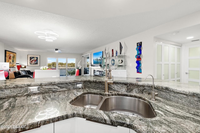 kitchen featuring white cabinetry, sink, a textured ceiling, and dark stone countertops