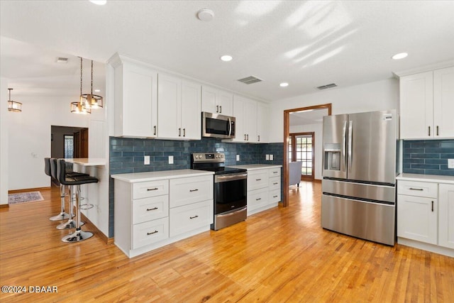 kitchen featuring stainless steel appliances, hanging light fixtures, a breakfast bar, white cabinetry, and light wood-type flooring