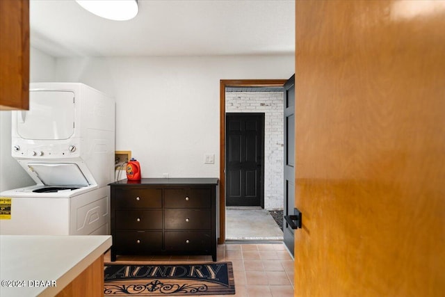 laundry room featuring stacked washing maching and dryer, cabinets, and light tile patterned floors