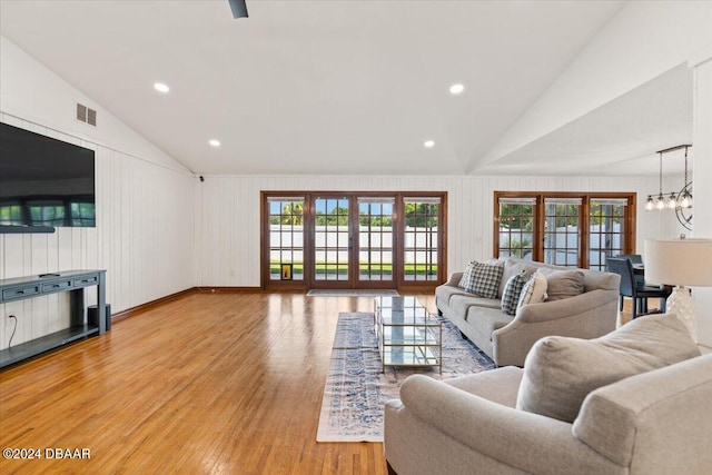 living room featuring french doors, light hardwood / wood-style floors, vaulted ceiling, and an inviting chandelier