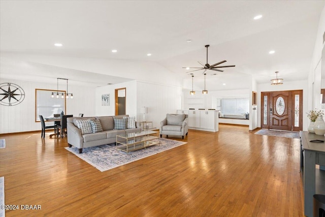 living room with light hardwood / wood-style floors, ceiling fan with notable chandelier, and vaulted ceiling